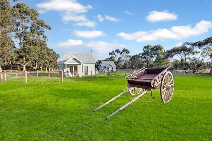 A rustic timber cart on the green paddock at Eagle Point Cottages, with a cottage beyond