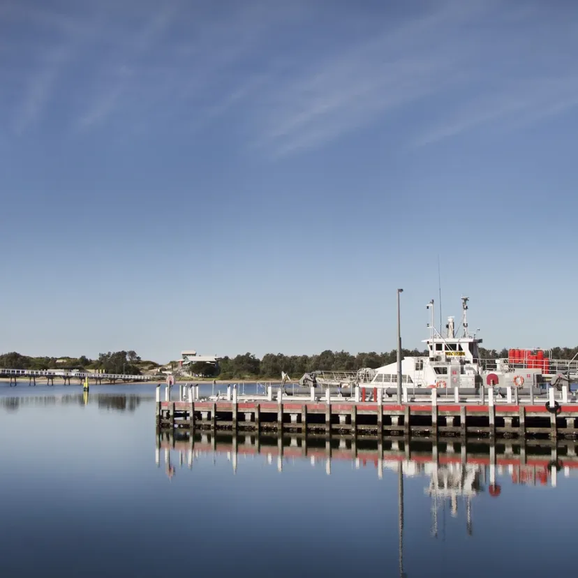 Fishing boats moored along a timber wharf on mirror calm water