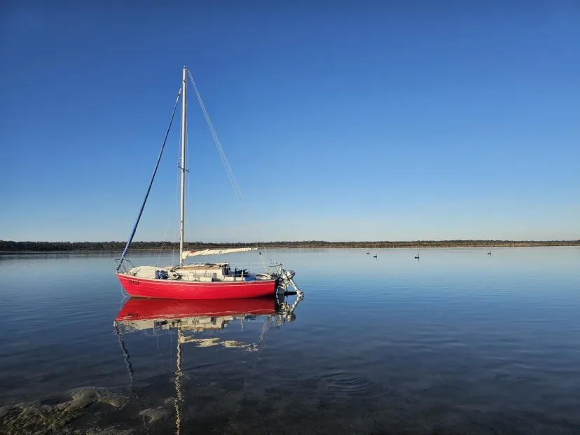 A red yacht moored on calm, clear water on the Gippsland Lakes.